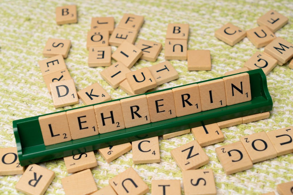 Wooden Scrabble tiles spelling 'Lehrerin' on a green holder, scattered on a textured surface.